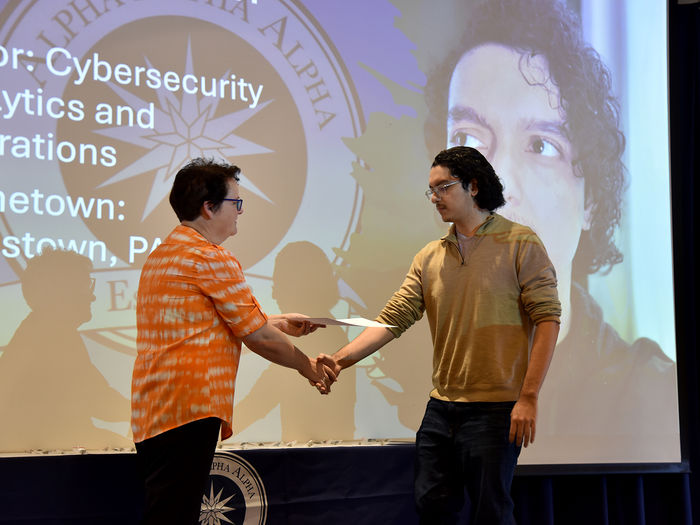 Hans Esteban, cybersecurity analytics and operations major, accepts his certificate and pin at the induction ceremony. 
