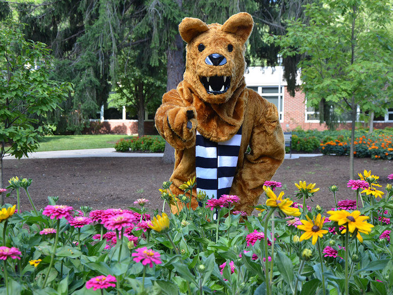 The Nittany Lion posing behind a clump of flowers